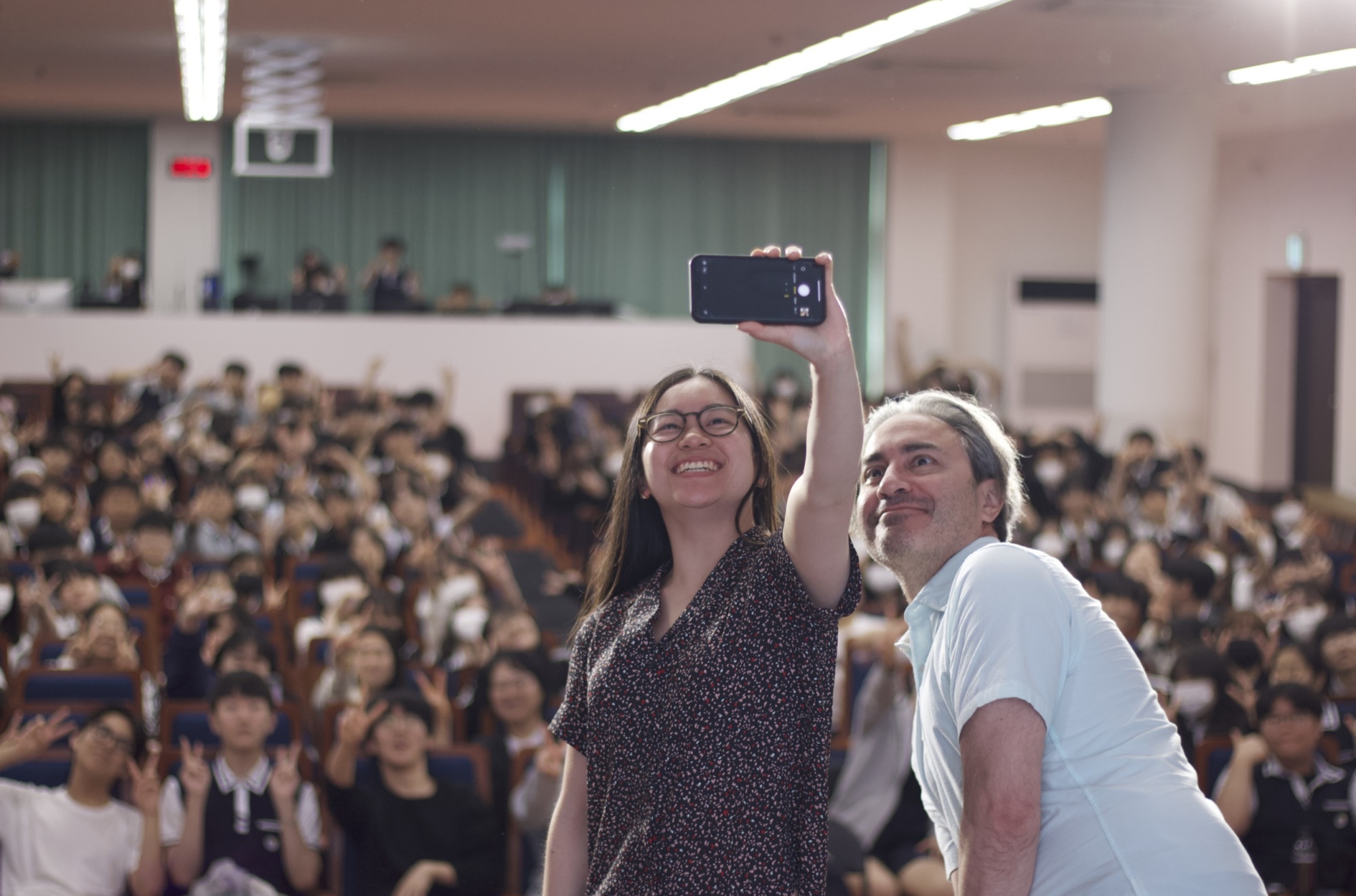 Two people on a stage taking a selfie with the audience